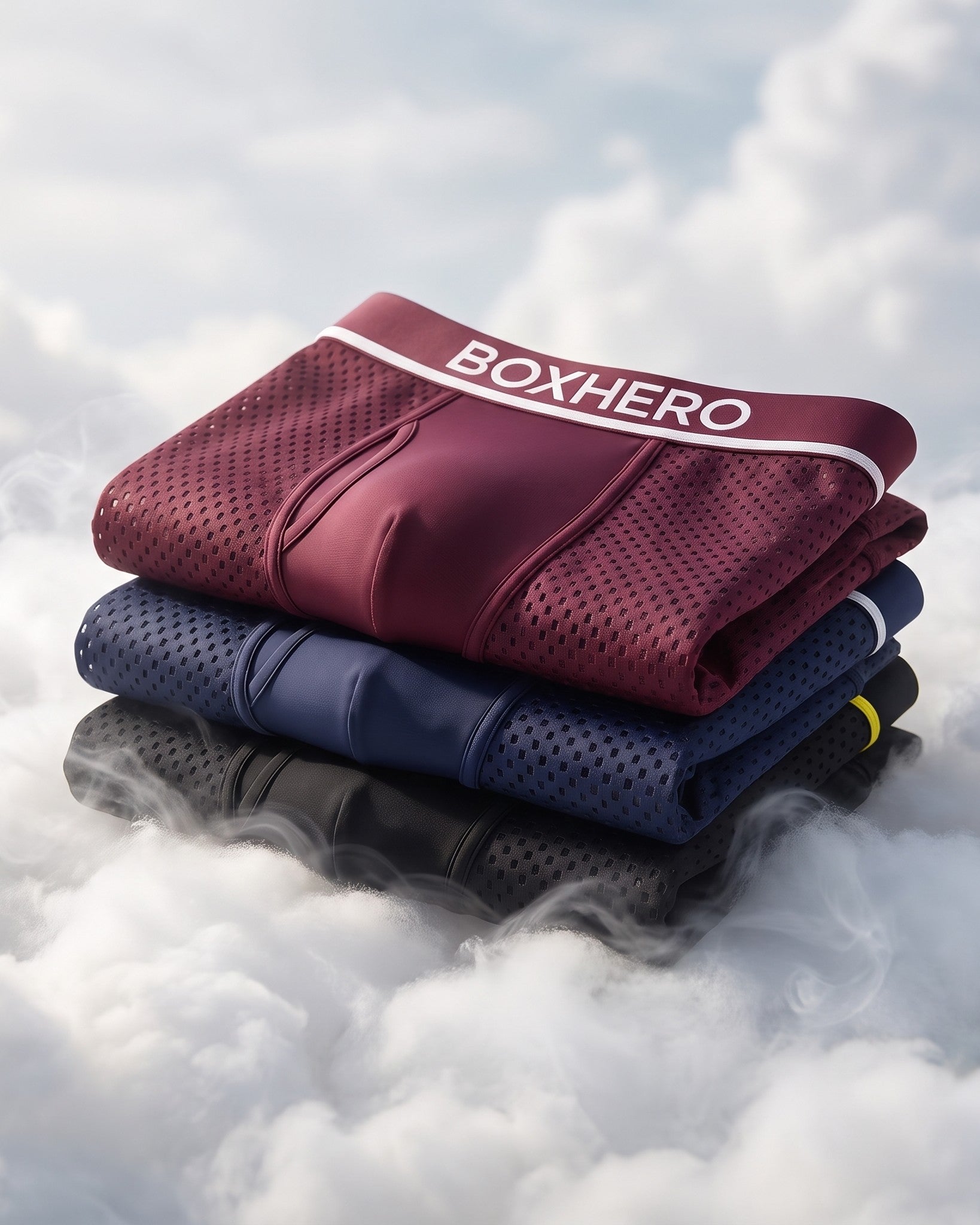 A stack of folded BoxHero 2.0 boxer briefs in burgundy, navy and black resting on soft clouds